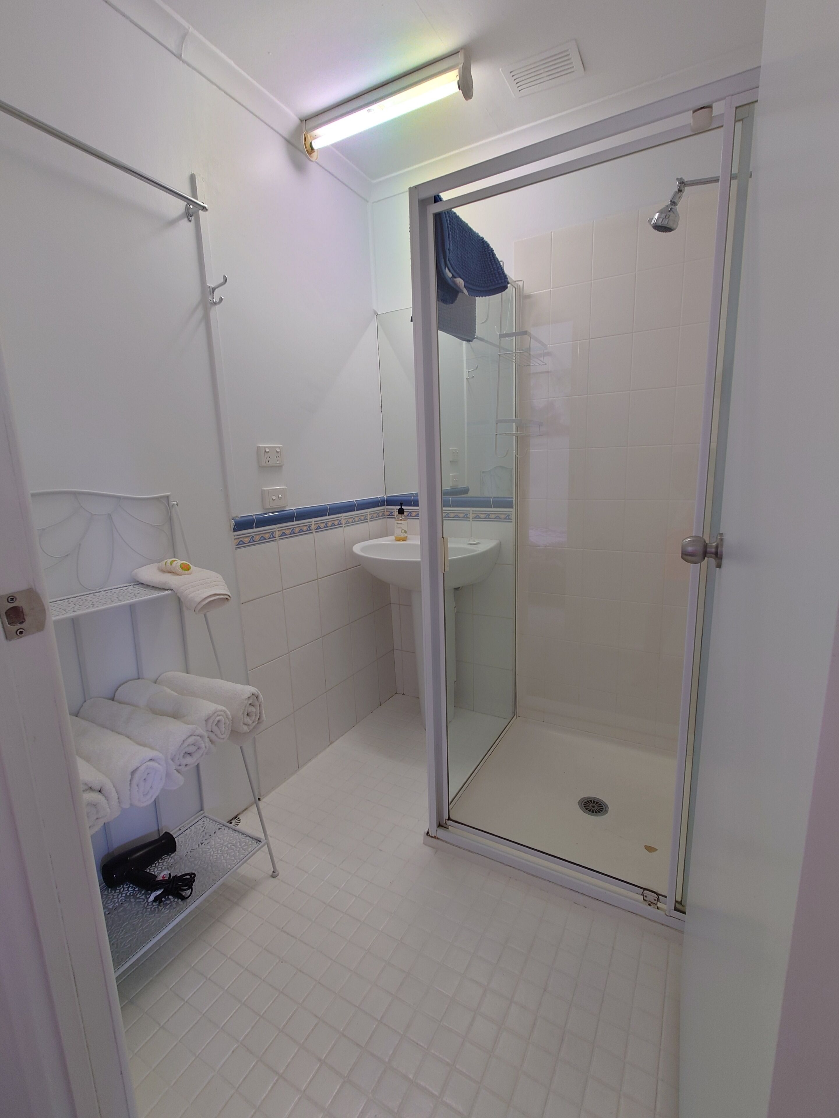 A bathroom with a glass-enclosed shower, a sink, and a towel rack with neatly folded towels.