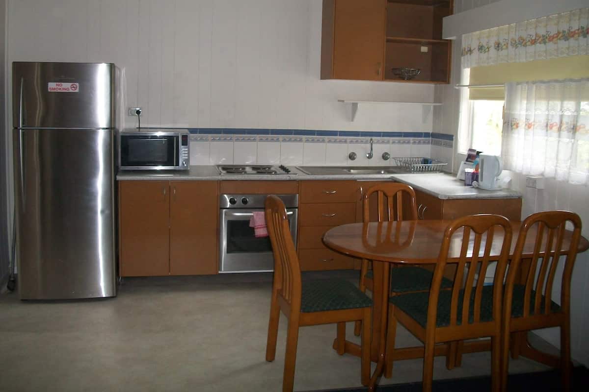 A compact kitchen with a refrigerator, microwave, stove, and sink. There is a dining table with chairs.