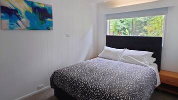 A bedroom with a bed, a window, and a painting on the wall.