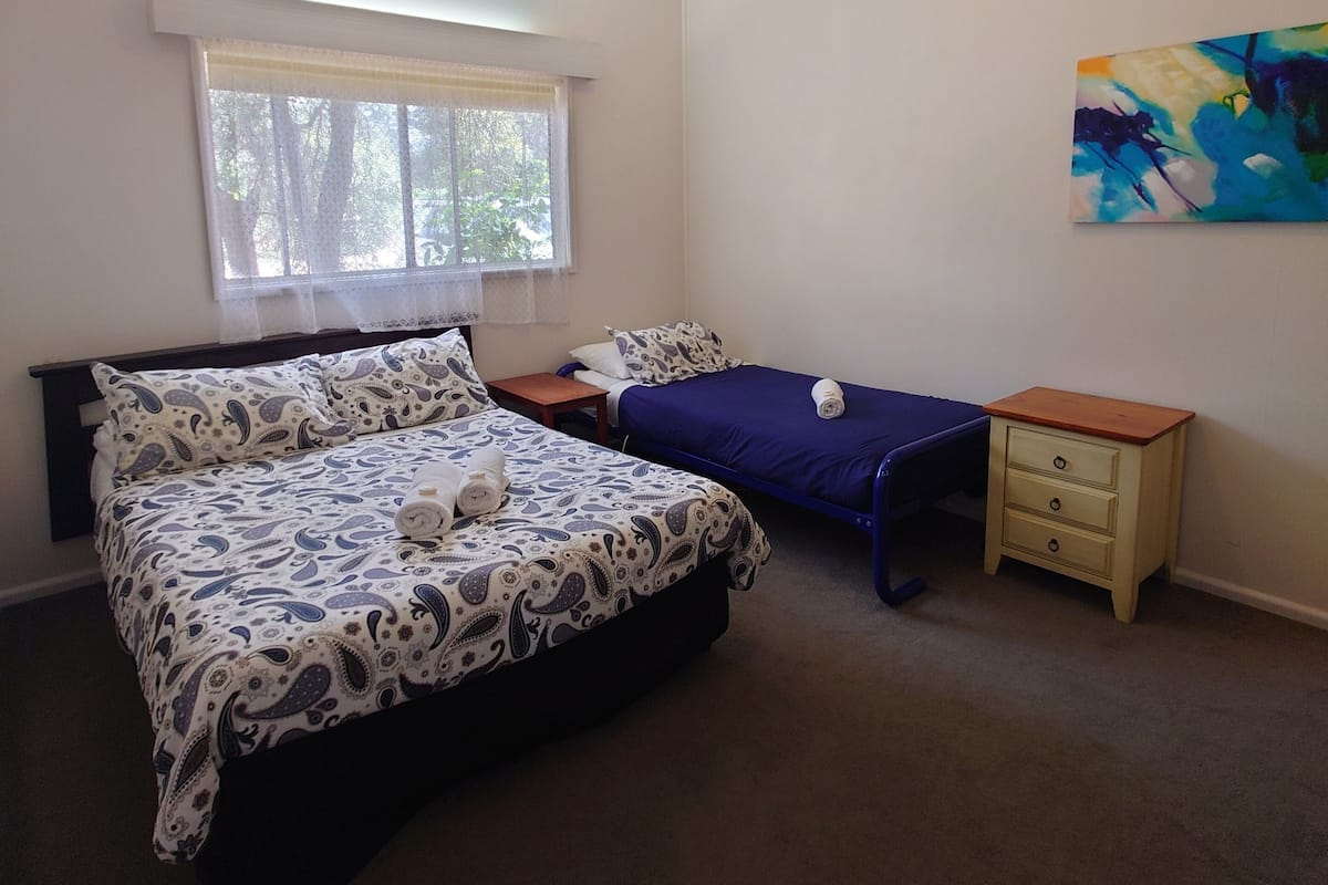 A bedroom with a large bed, a smaller bed, a nightstand, a window with curtains, and a ceiling light.