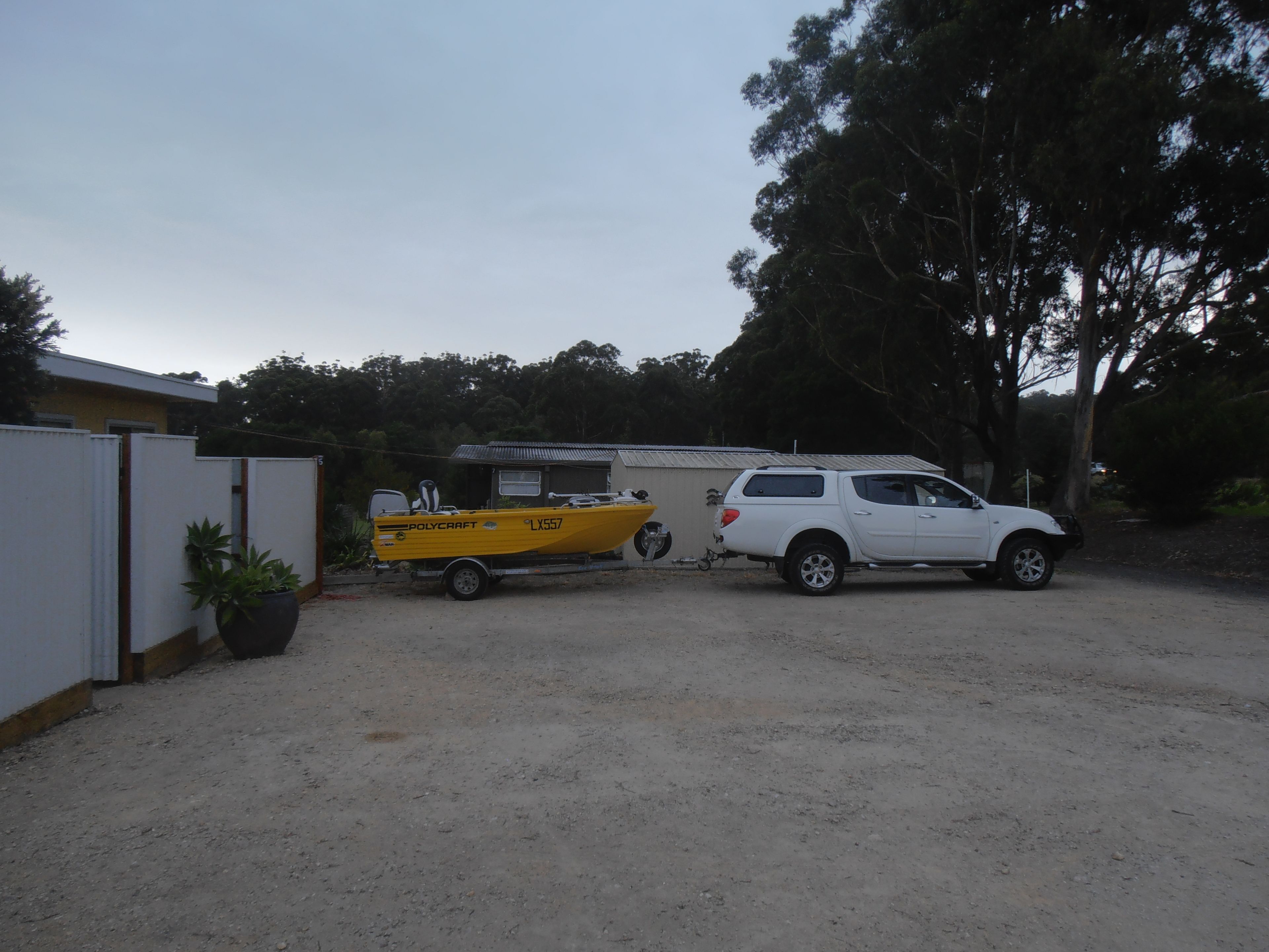 A white SUV parked in a gravel driveway next to a yellow boat trailer with a boat.