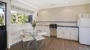 Cocina compacta con armarios blancos, una mesa de comedor de vidrio y vistas a zonas verdes.