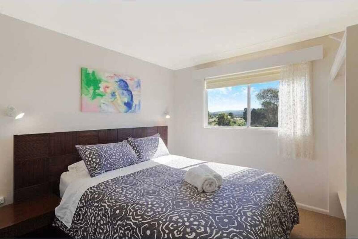 A bedroom with a large bed, a window with curtains, and a painting on the wall.
