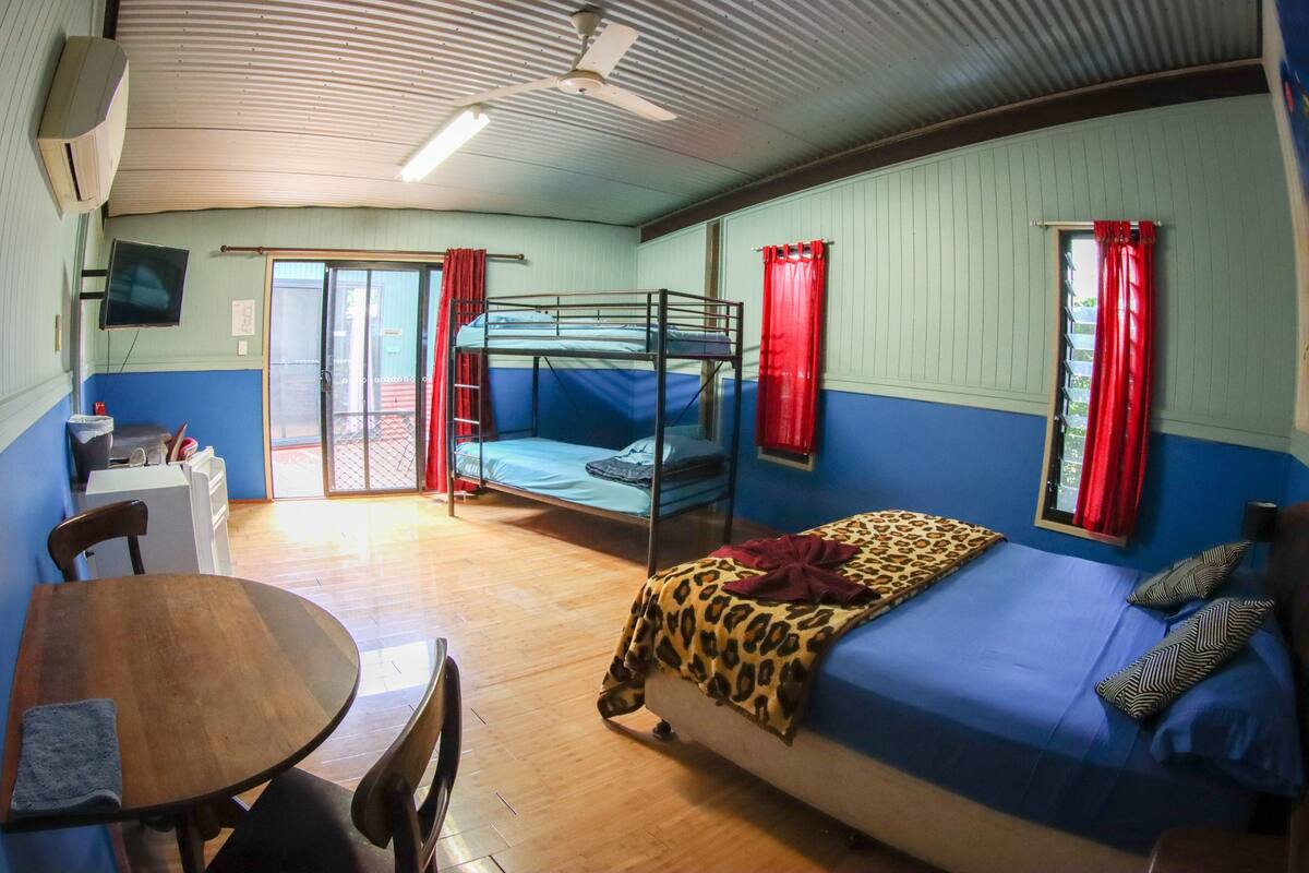 A dormitory room with bunk beds, a dining table, and a television.