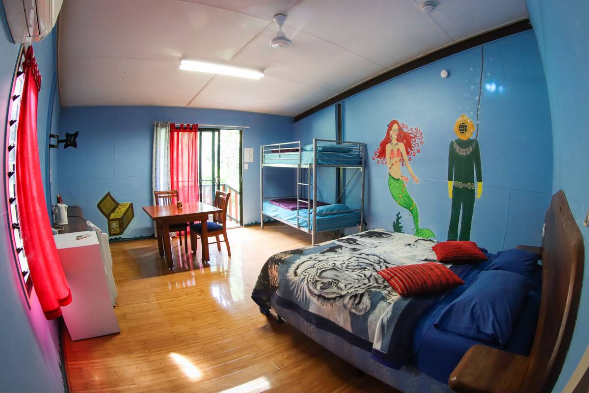 A room with bunk beds, a dining table, chairs, a refrigerator, and a mural on the wall.