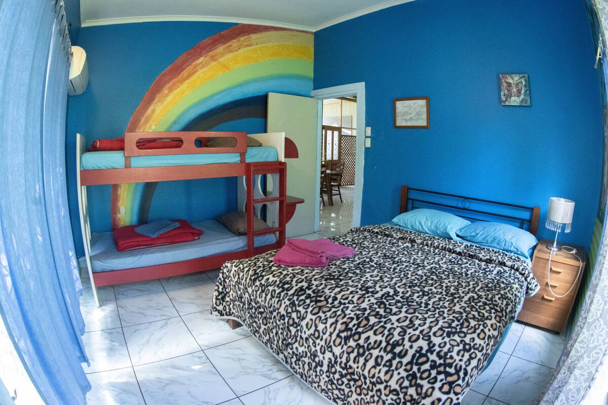 A bedroom with a bunk bed, a large bed with a leopard print cover, a nightstand with a lamp, and a rainbow mural on the wall.