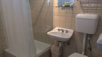 A bathroom with a shower, sink, toilet, and a glass shelf with toiletries.