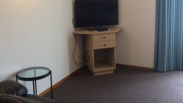 A living room with a flat-screen TV on a wooden stand, a small round table, a leather sofa, and a blue curtain.