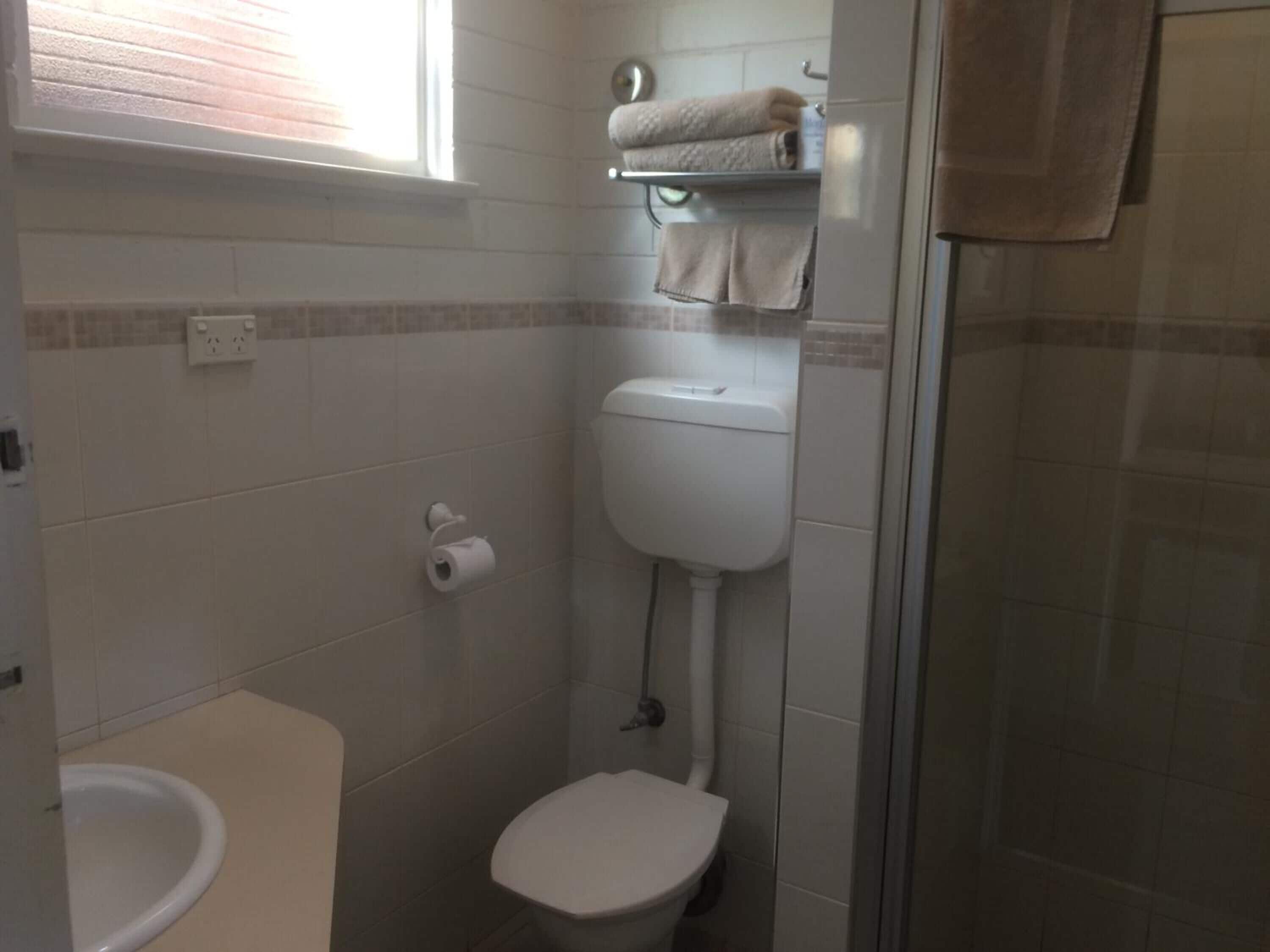 A small bathroom with a toilet, a towel rack, and a shower area.