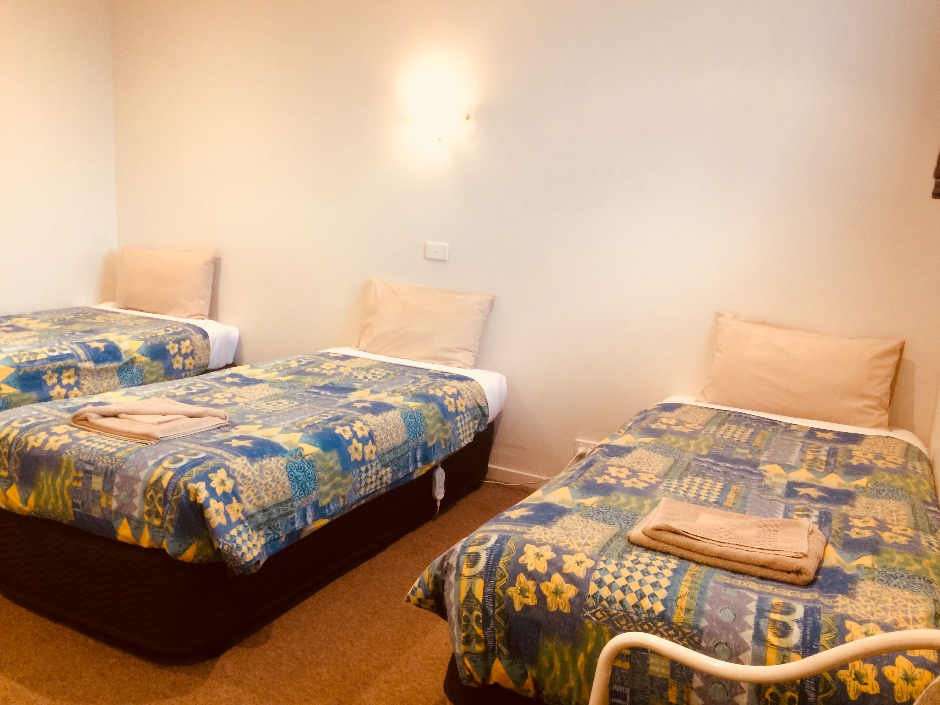 A room with two single beds, each with a patterned bedspread and a folded towel.
