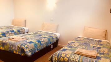 A room with two single beds, each with a patterned bedspread and a folded towel.
