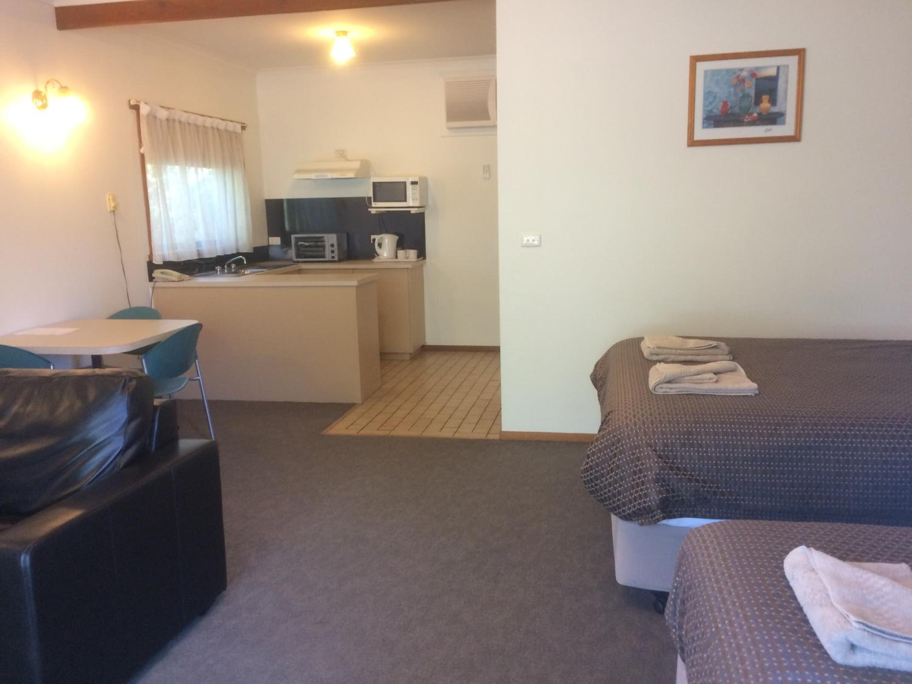 Una habitación de hotel compacta con kitchenette, comedor y cama.