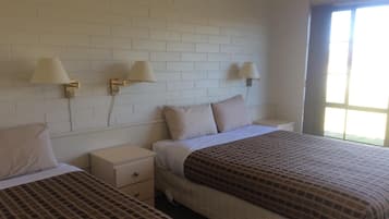 A hotel room with two beds, white brick walls, and wall-mounted lamps.