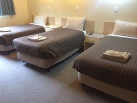 Habitación de hotel con dos camas individuales, cada una con una almohada y una toalla doblada. Hay una mesita de noche entre las camas con un control remoto encima.
