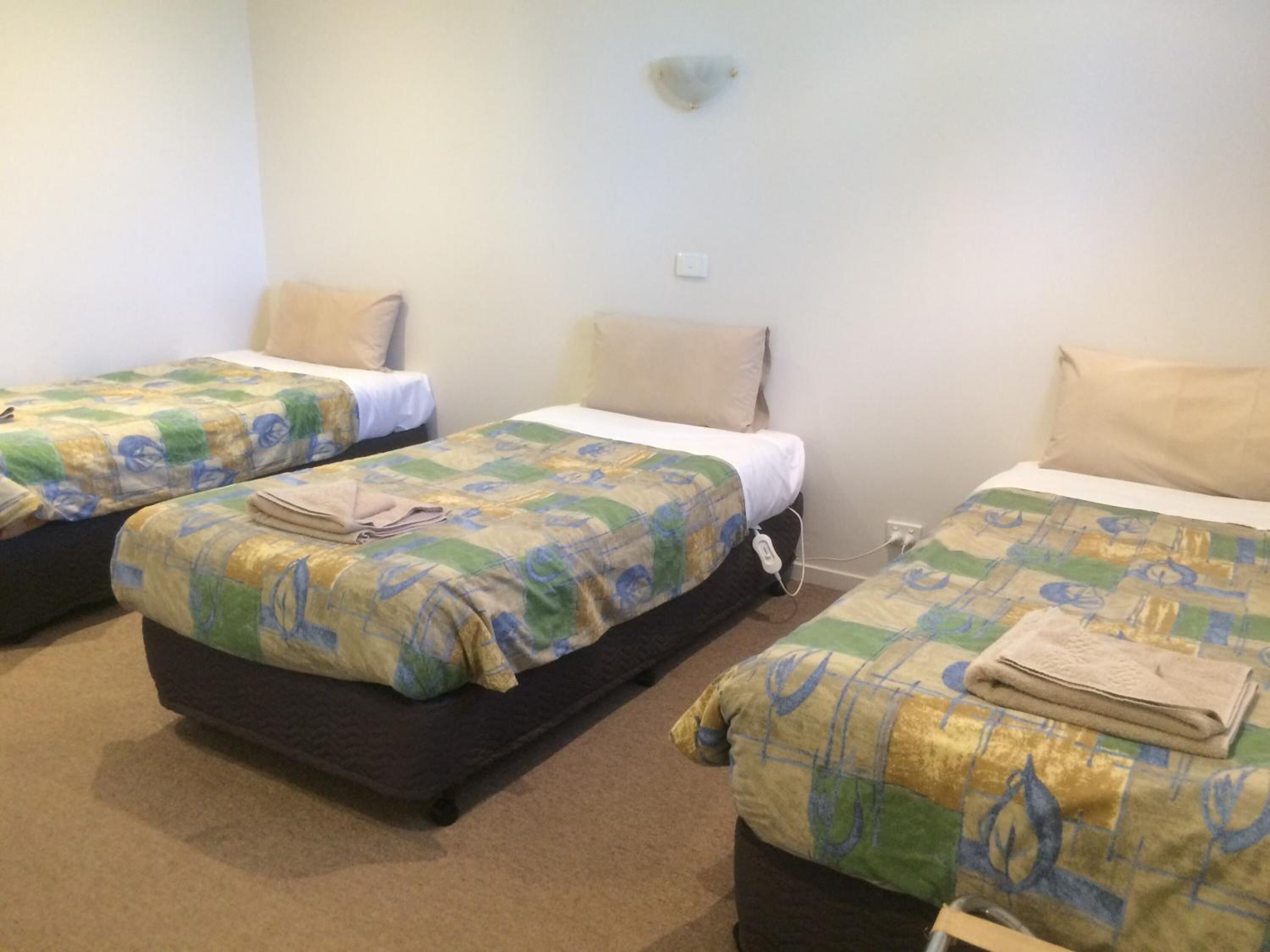 A room with three beds, each with a patterned bedspread and a folded towel on top.