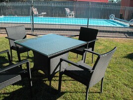 Un área de estar al aire libre con una mesa y sillas, una piscina al fondo y una valla.