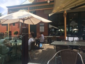 An outdoor café with tables and chairs, umbrellas, and a brick building in the background. - Ambassador Motor Inn Ballarat (Alfredton)