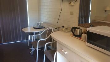 A small kitchenette with a microwave, kettle, and phone. There is a table and two chairs in the room.