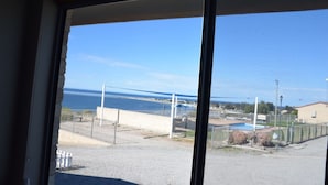 A view through a window of a coastal area with a beach, a fence, and a building in the background. - Stansbury Holiday Motel (Stansbury)
