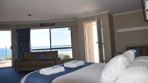 A hotel room with a bed, a sofa, and a large window offering a view of the sea. - Stansbury Holiday Motel (Stansbury)
