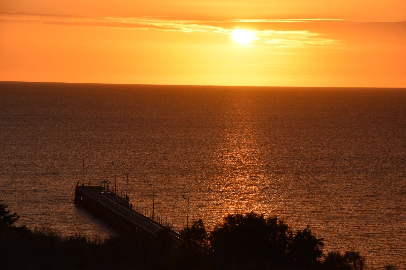A sunset over a body of water with a bridge in the foreground.