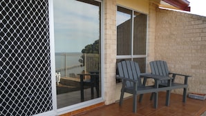 A patio with two Adirondack chairs, a small table, and a view of the sea through a large glass door. - Stansbury Holiday Motel (Stansbury)