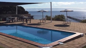 A swimming pool with a view of the sea, outdoor seating, and a covered area. - Stansbury Holiday Motel (Stansbury)