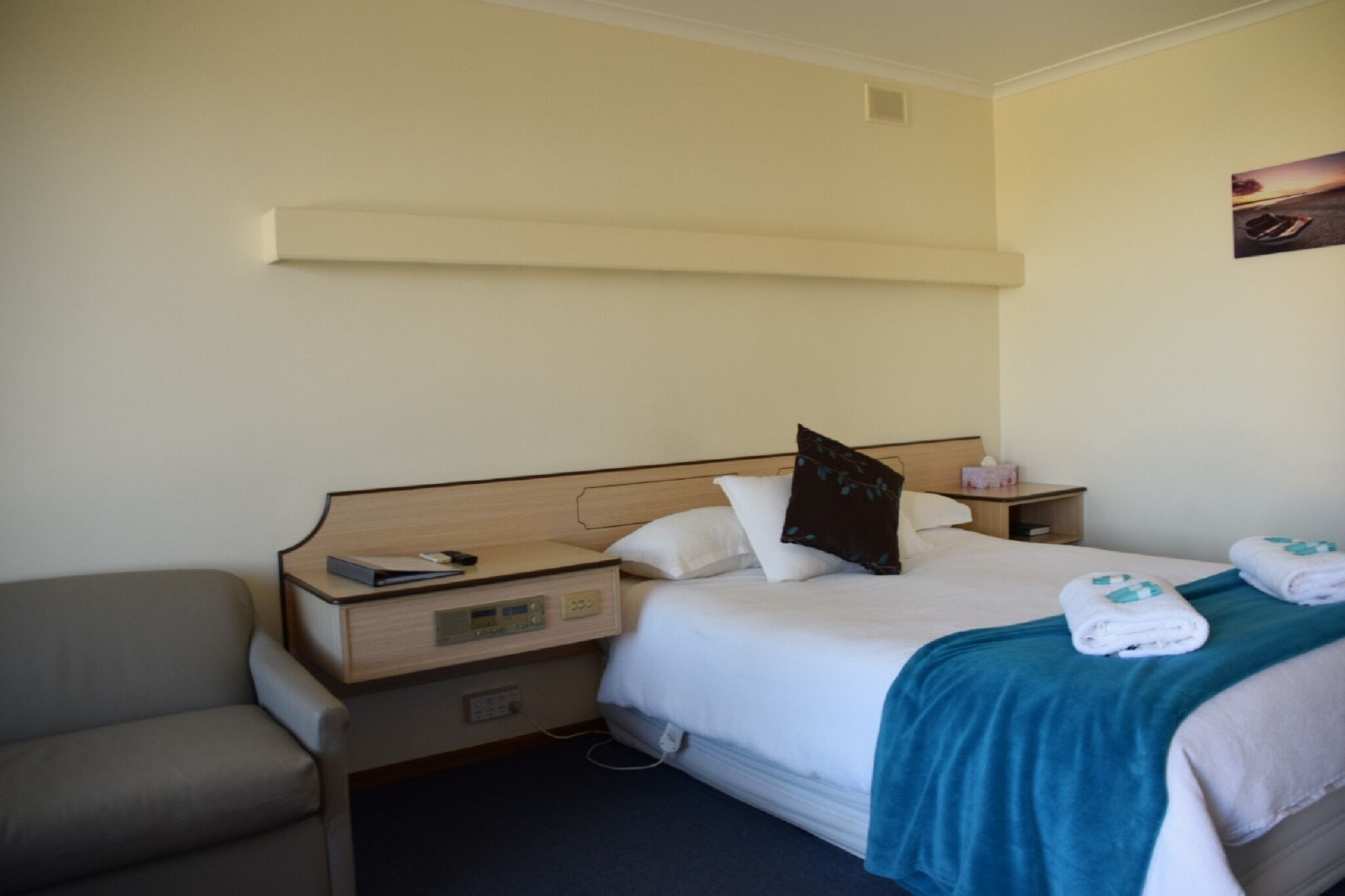 A hotel room with a bed, bedside tables, a chair, and a painting on the wall.
