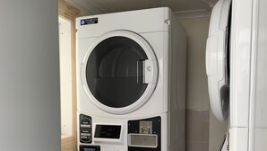 Une machine à laver et un sèche-linge superposés dans une buanderie, avec un panneau de commande visible et un luminaire au plafond.