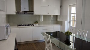 Une cuisine moderne avec des meubles blancs, une cuisinière à gaz et une table à manger en verre.