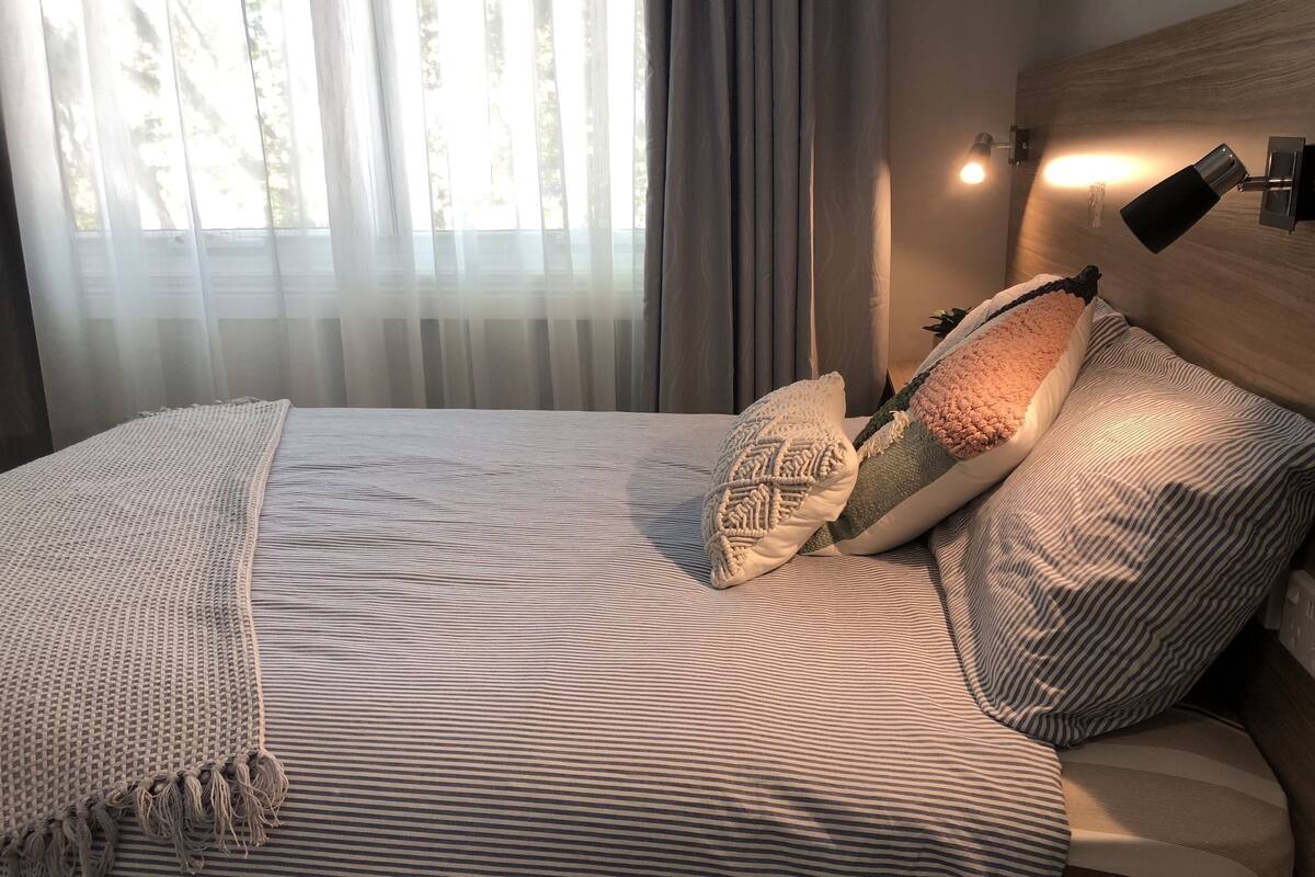 A neatly made bed with striped bedding and a woven throw blanket.