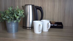 Une cafetière en acier inoxydable, deux tasses blanches, une plante en pot et une boîte de thé, le tout posé sur une surface en bois.