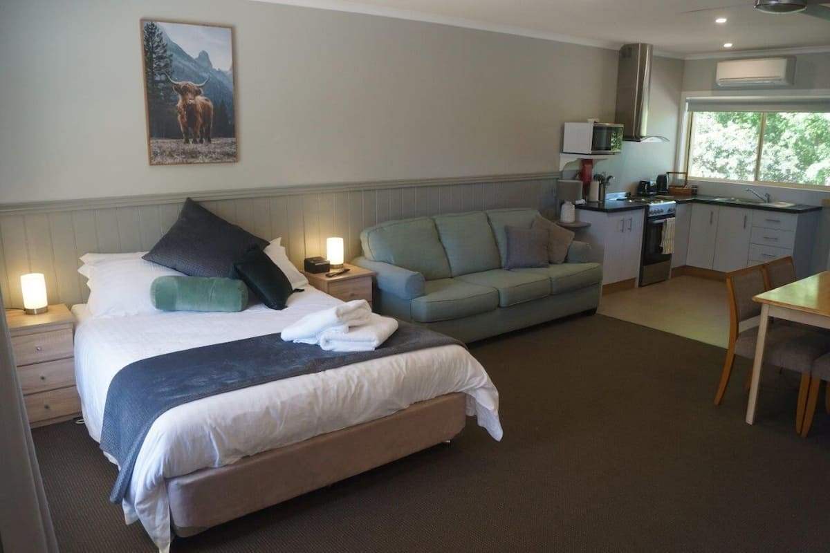 Una habitación de hotel con cama, sofá, mesa de comedor, kitchenette y un cuadro en la pared.