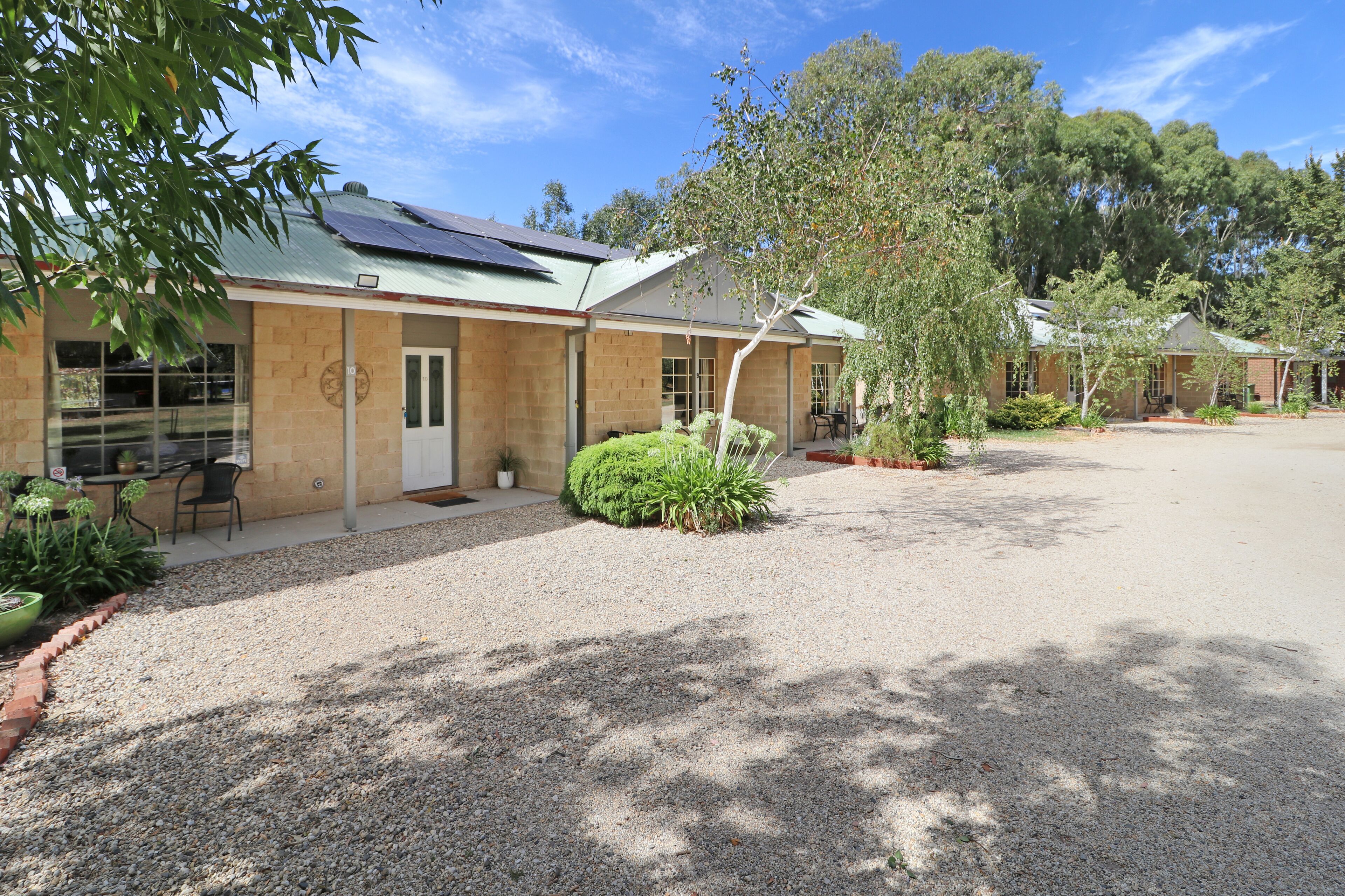 A building with a gravel driveway, a covered outdoor seating area, and a solar panel on the roof.