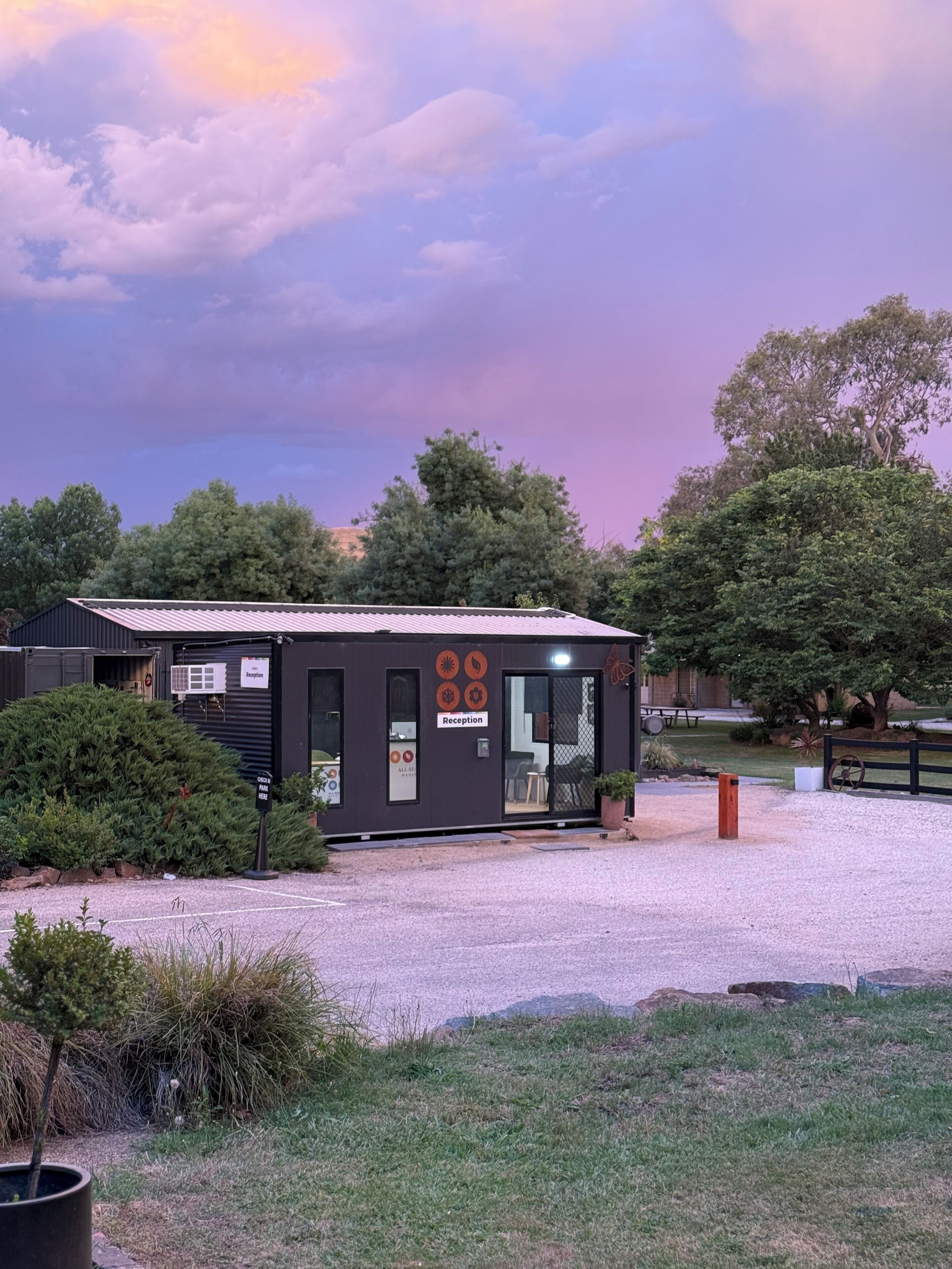A small building with a reception area, surrounded by trees and a gravel path.