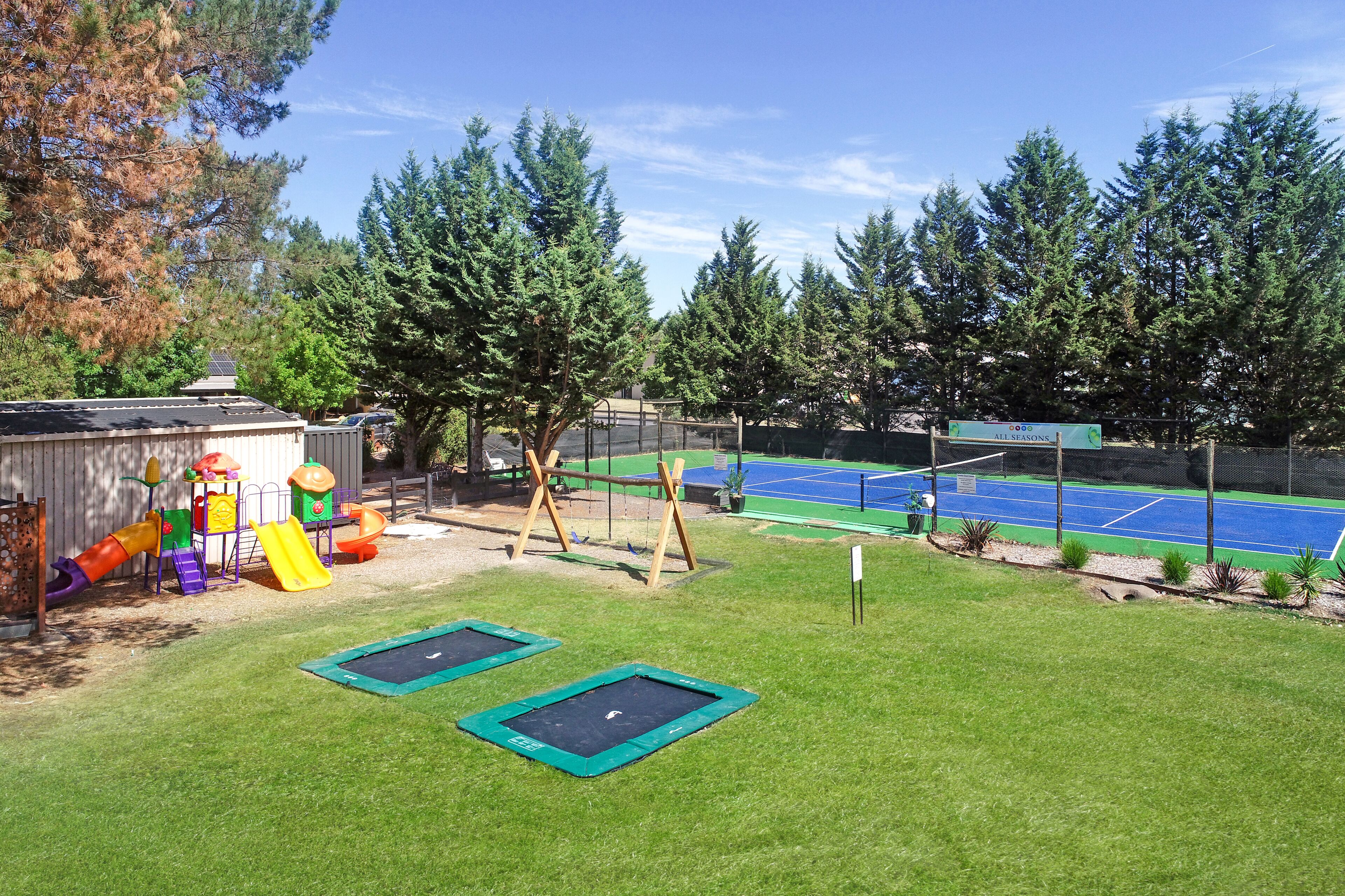 Un patio trasero con un trampolín, un parque infantil y una cancha de tenis.