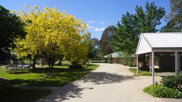 A gravel path leading to a covered pavilion with a white roof, surrounded by green grass and trees with yellow foliage.