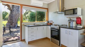 Una cocina con armarios blancos, estufa, microondas y ventana con vistas a un jardín.