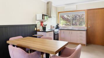 A compact kitchen with a wooden table and pink chairs, a microwave, and a stove.