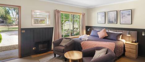 A bedroom with a bed, two armchairs, a small table, a nightstand, and a fireplace.