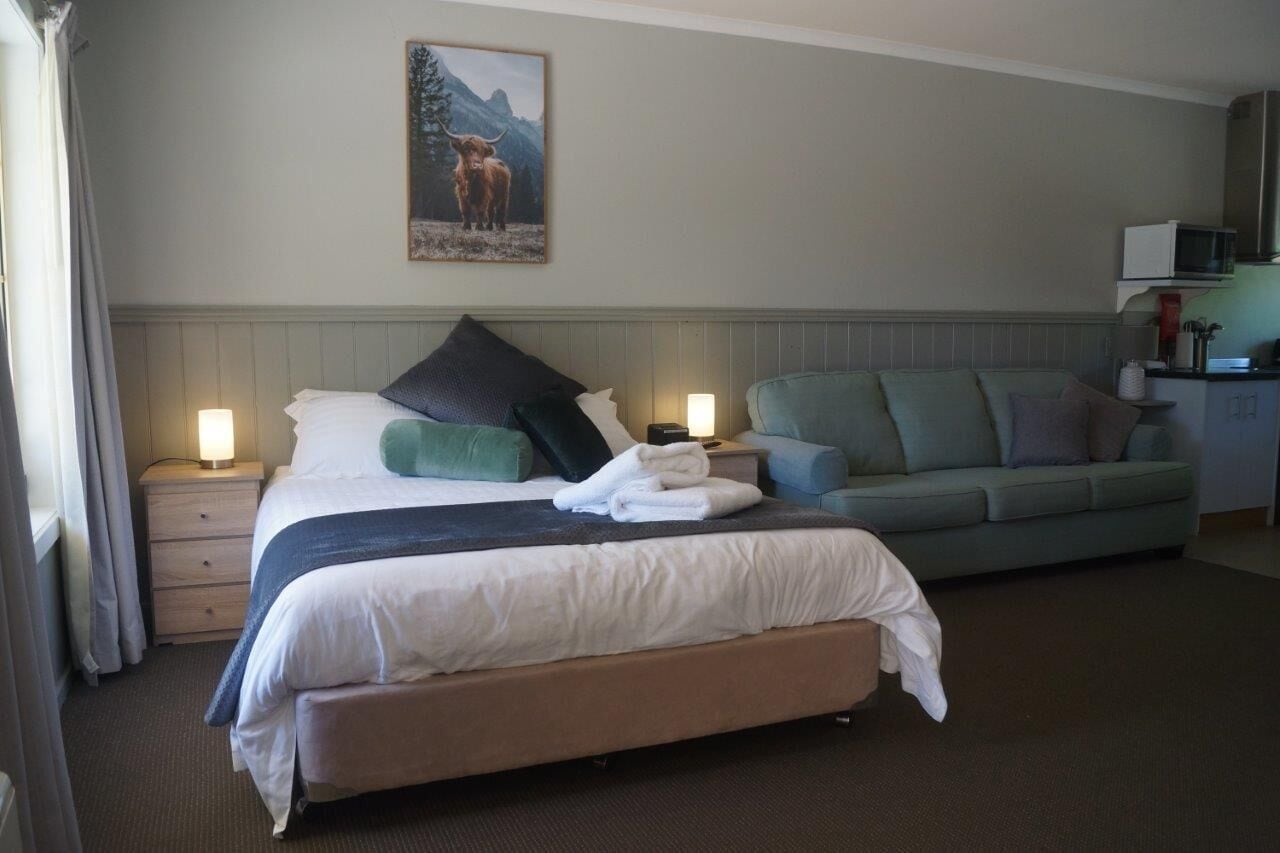 A hotel room with a bed, a sofa, a nightstand, a lamp, and a painting on the wall.