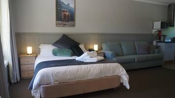 A hotel room with a bed, a sofa, a nightstand, a lamp, and a painting on the wall.