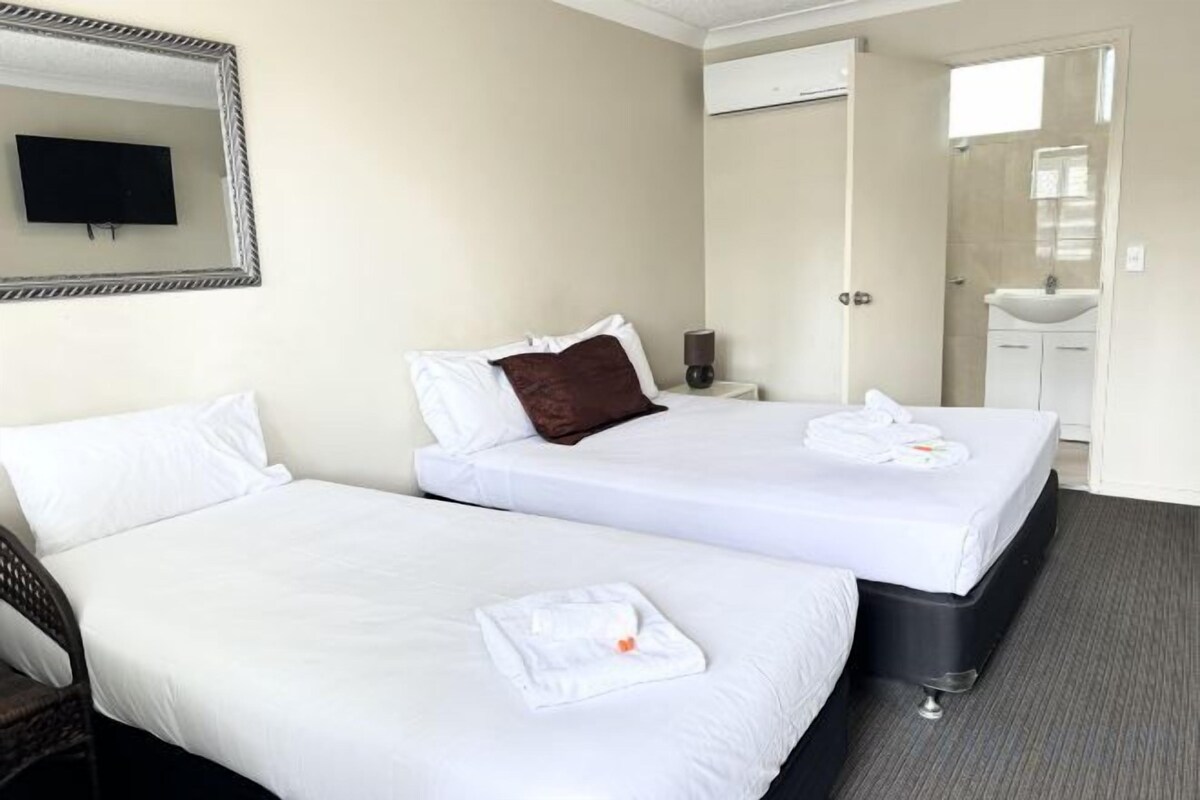 A hotel room with two beds, a TV, a bathroom with a sink, and a mirror.