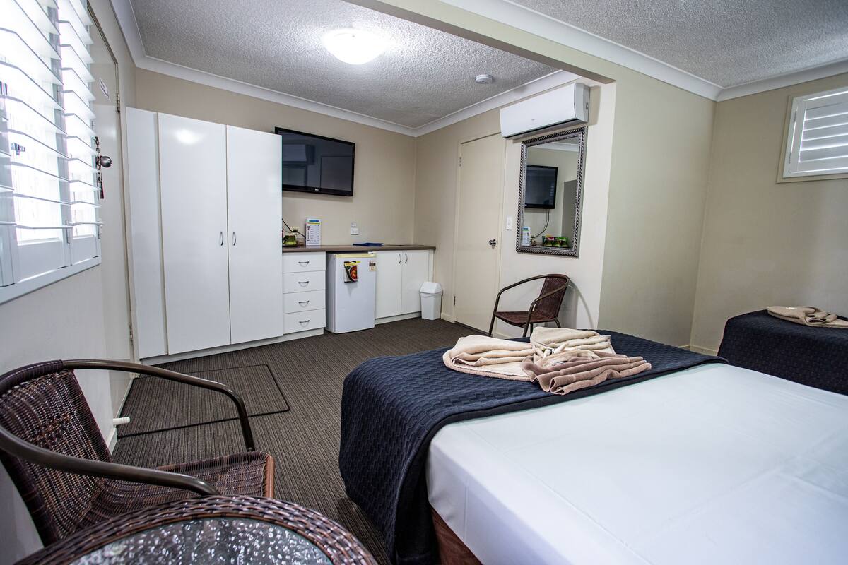 Ein Hotelzimmer mit Bett, Schreibtisch, Stuhl, Kleiderschrank, einer kleinen Küchenzeile und einem Spiegel.
