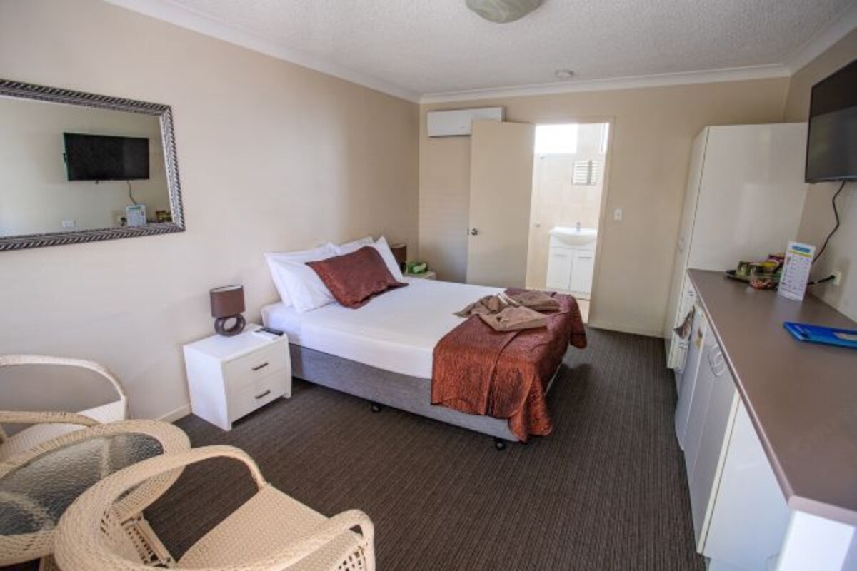 A hotel room with a bed, bedside table, lamp, and a desk with a chair.
