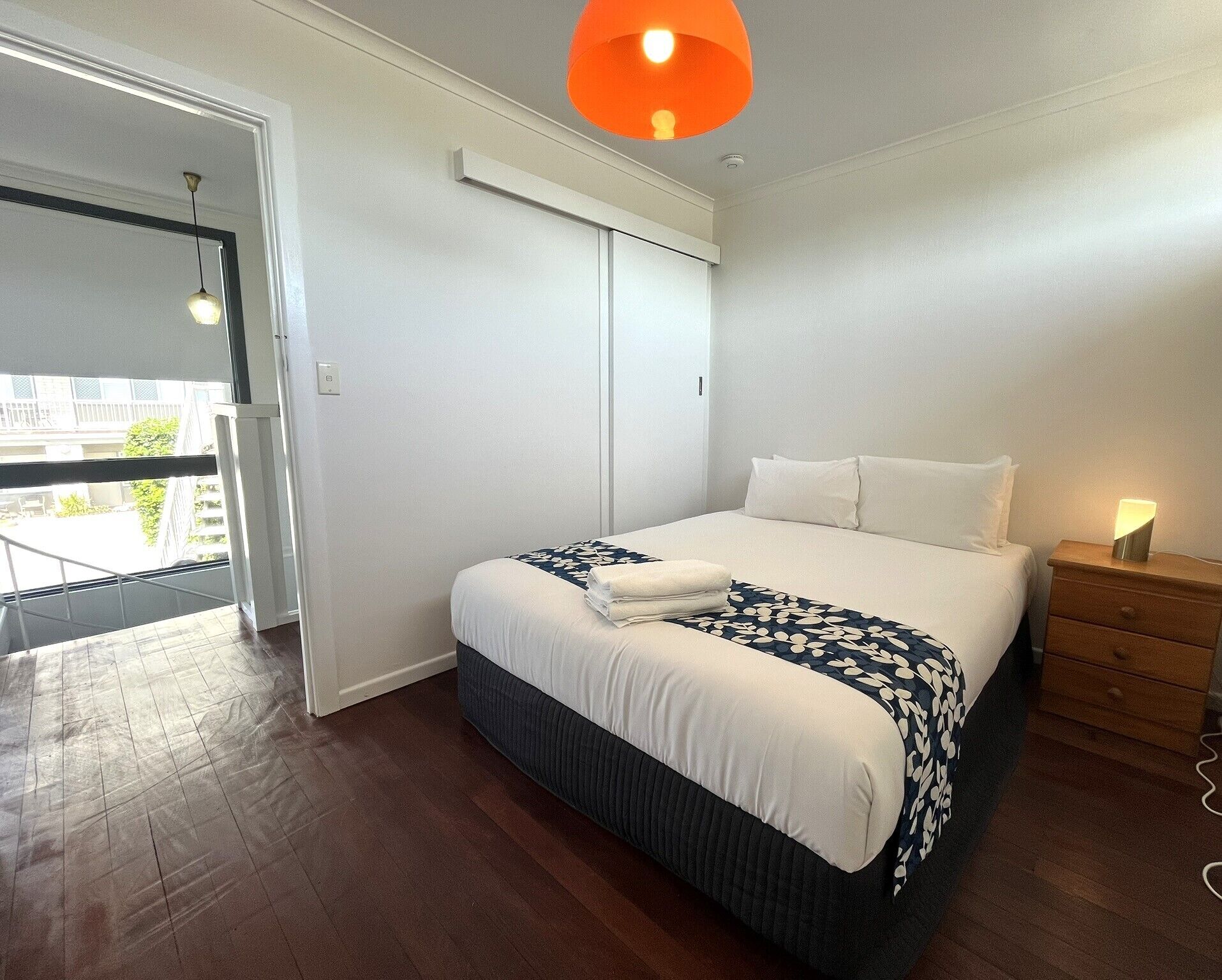 A bedroom with a bed, a nightstand, a window, and a door leading to a balcony.
