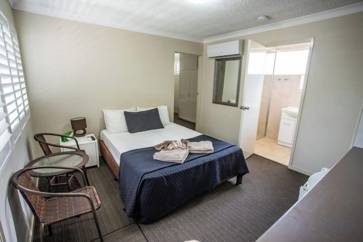 A hotel room with a bed, a chair, a desk, and a bathroom door.