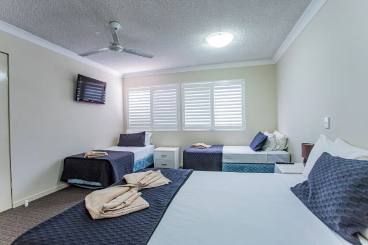 A hotel room with a bed, two bedside tables, a ceiling fan, and a window with blinds.