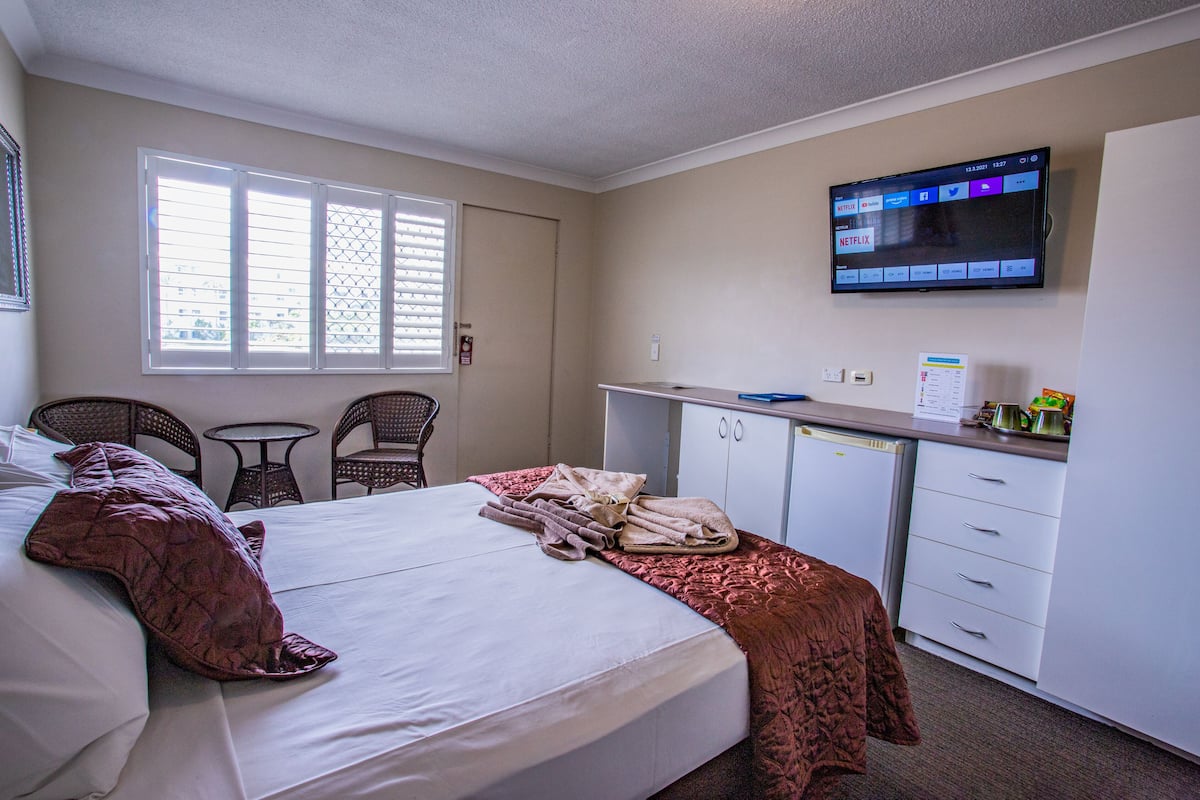 Ein Hotelzimmer mit einem Bett, einem Schreibtisch, einem Stuhl und einem an der Wand befestigten Fernseher.