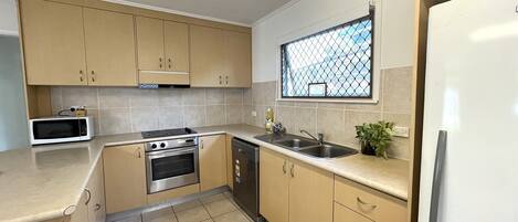 Una cocina compacta con armarios color beige, un microondas, un horno, un lavavajillas y un refrigerador.